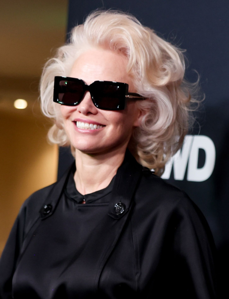 Pamela Anderson smiling in sunglasses and black coat